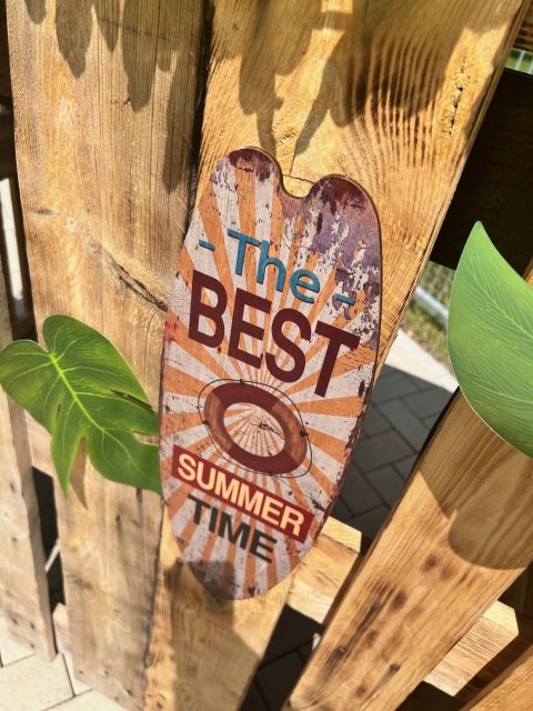 Holzaufsteller mit der Aufschrift The best summer time lehnt an einer Holzwand