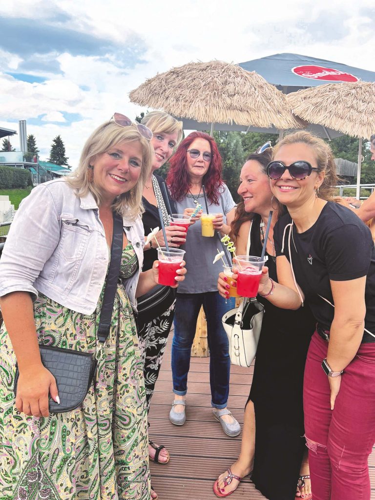 fünf Frauen stehen mit Cocktails an einer Strandbar