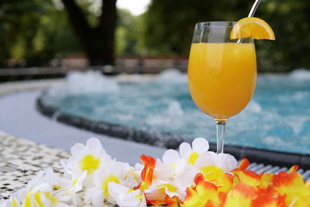 gelber Cocktail mit Blumenkette und einem Whirlpool im Hintergrund